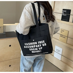 Detail of black canvas tote bag showing metal snap closure and white printed text design