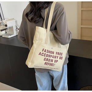 Detail of off-white canvas tote bag with red typography in a casual cafe setting