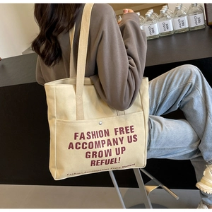 Detail of beige canvas tote bag showing the front button pocket and red slogan print