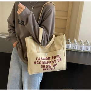 Detail of canvas tote bag showing red fashion slogan print and thick woven shoulder strap