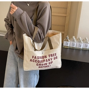 Close-up of off-white canvas tote bag with retro red lettering and brown straps