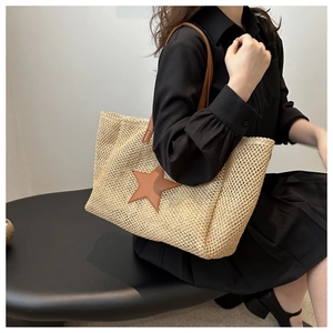 Detailed view of woven straw tote bag featuring a brown leather star and slender shoulder straps