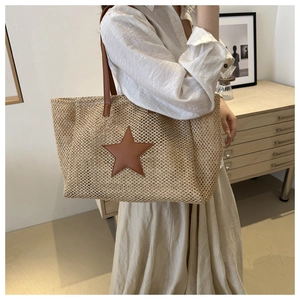 Detail of hand-woven straw tote bag with brown leather star patch and shoulder strap