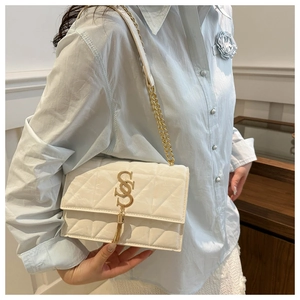 Detail of white quilted flap bag with golden chain strap and tassel metal buckle