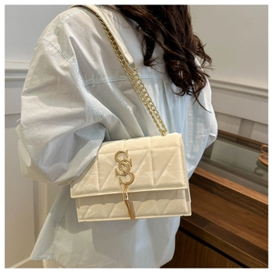 Detail view of cream-white quilted crossbody bag with gold S-buckle and tassel chain