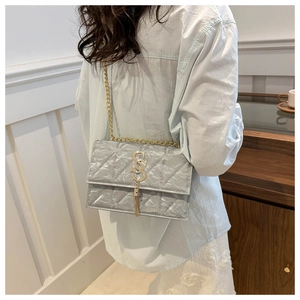 Detail of silver quilted chain bag with gold SS logo and elegant metallic tassel charm