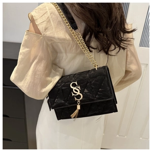 Close-up of black quilted crossbody bag featuring a golden S logo and fringe chain strap