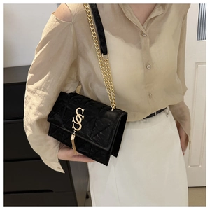 Detail of black quilted shoulder bag featuring gold S-shape clasp and elegant tassels