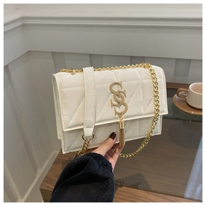 Detail of white quilted handbag with gold SS logo and chain strap on a wooden table