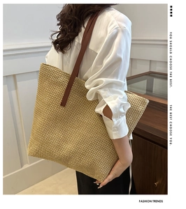Side view of a large woven tote bag with brown leather straps and fine raffia texture