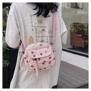 Outdoor shot of pink corduroy small crossbody bag with red strawberry print detail