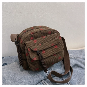 Detail of dark brown corduroy crossbody bag with red strawberry pattern on denim background