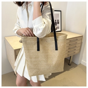 Detail of hand-woven straw tote bag showing fine texture and sleek black leather straps