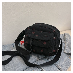 Close-up of black corduroy shoulder bag featuring red strawberry prints and buckle pocket