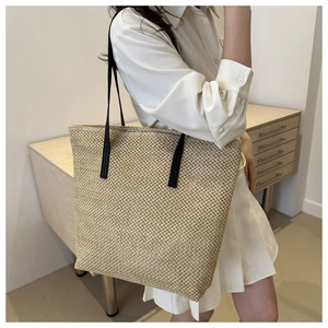 Side view of large beige woven tote bag with slim black straps on model shoulder