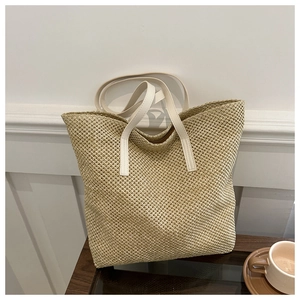 Close-up of woven straw tote bag with white leather straps on a wooden tray