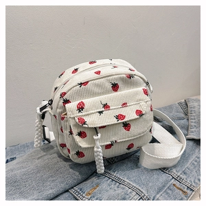 Close-up of white corduroy crossbody bag with red strawberry print on denim background