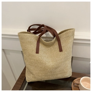 Detail of woven straw tote bag with brown leather handles on a minimalist table
