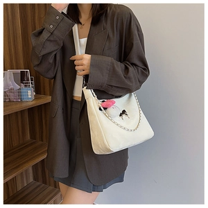 Detail of white minimalist crescent bag with dual straps and plush pendant