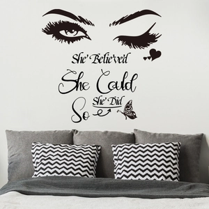 Détail de sticker mural noir avec cils, papillons et texte de motivation sur un mur blanc