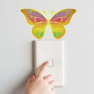 Detailopname van een glitter regenboog vlinder muursticker op een witte lichtschakelaar