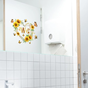 Détail d'un autocollant WC avec tournesol, cœur doré et papillon sur carreaux blancs