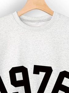 Close-up of 1976 print on heather grey crewneck sweatshirt hanging on wooden hanger
