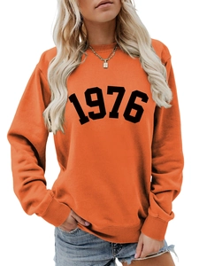 Detail of the orange sweatshirt showing the bold 1976 print and ribbed neckline