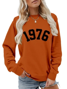 Close-up of ribbed cuffs and black 1976 vintage print on orange long sleeve sweatshirt