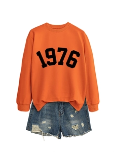 Detail of orange sweatshirt with black 1976 print paired with distressed denim shorts