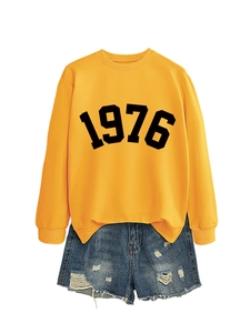 Detail view of yellow crewneck sweatshirt featuring black 1976 print and ripped denim shorts