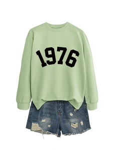 Close-up of light green 1976 printed sweatshirt with distressed denim shorts detail