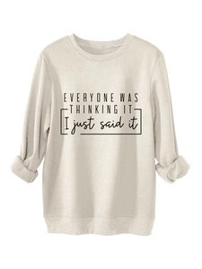 Detalle de sudadera beige con estampado de eslogan negro y puños acanalados