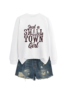 Flat lay of a white sweatshirt with 'Just a Small Town Girl' text and ripped denim shorts