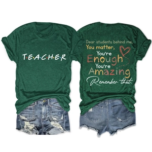 Flat lay of teacher t-shirt showing front text and back student quote on dark green cotton