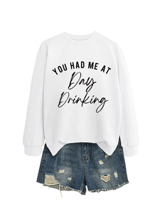 Flat lay of a white 'You Had Me At Day Drinking' sweatshirt and ripped denim shorts