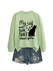 Flat lay of light green sweatshirt with cat slogan print and distressed denim shorts