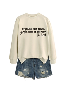 Detail of cream sweatshirt with black slogan print paired with distressed denim shorts