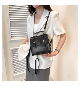 Chic black leather handbag with gold metal buckles shown on an elegant white suit
