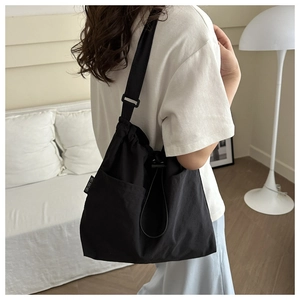 Minimalist black nylon drawstring tote bag with shoulder strap in a modern home setting