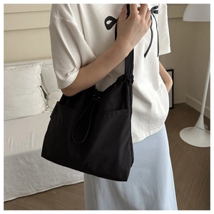 Close-up of black nylon shoulder bag featuring functional drawstring closure and side pockets