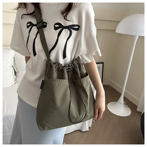 Detail of dark green nylon drawstring bucket bag featuring front utility pockets and strap