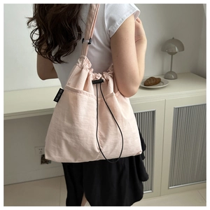 Close-up of light pink nylon drawstring bag showing the adjustable cords and woven label