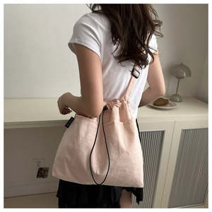 Detailed side view of pink canvas drawstring bucket bag with black adjustable shoulder strap