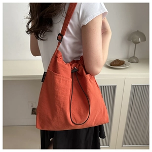 Detail of orange drawstring crossbody bag with side pockets and adjustable straps