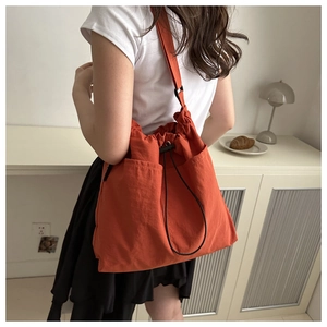 Detail view of orange nylon drawstring bucket bag with adjustable straps and side pocket