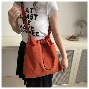 Close-up of lightweight nylon bucket bag in orange with drawstring and side brand label
