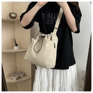 Detail of beige nylon drawstring bucket bag with adjustable strap and front pockets