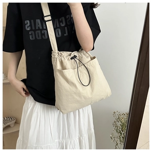 Detail view of beige nylon drawstring crossbody bag featuring a front pocket and adjustable strap