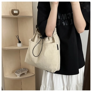 Detail of beige canvas tote bag with drawstring closure and large front pockets for storage
